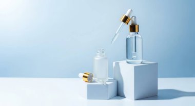 Beyaz küplerin üzerinde kozmetik şişeleri sergilenen zarif bir çekim, dingin mavi bir arkaplana karşı, geniş bir kopya alanı sunuyor. Güzellik ve cilt ürünlerini sergilemek için ideal.