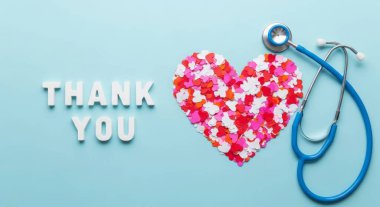 A thank you message to doctors and nurses with a stethoscope and heart shape made of flower petals on a blue background. Flat lay, top view. Thank you heroes!