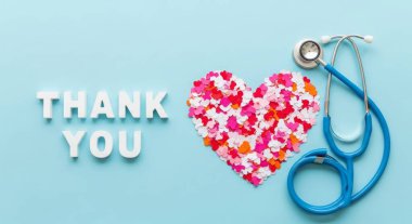 A heartfelt thank you message with a heart shape made of colorful confetti and a stethoscope on a blue background. Top view, flat lay composition. Expressing gratitude and appreciation.
