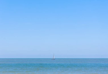 Yelkenli açık okyanus sularında güneşli bir gökyüzüne karşı süzülür..