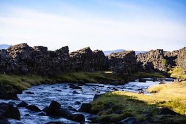 İzlanda manzarası. Kayalık bir kıyı şeridi ve arkasında bir dağ olan bir nehir. Su berrak ve sakin.