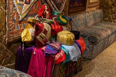 Masada renkli bir şapka ve eşarp gösterisi. Şapkalar çeşitli şekil ve boyutlarda ve eşarplar farklı renklerde. Sahne sıcak ve davetkar bir atmosfer yaratıyor.