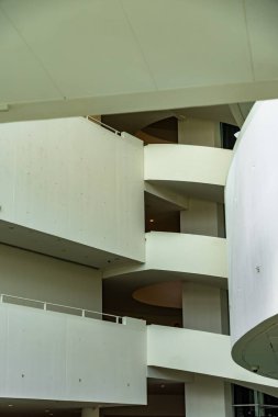 Modern bir binada katmanlı balkonları ve hafif ışıklandırması olan kıvrımlı beyaz mimari iç mekan..