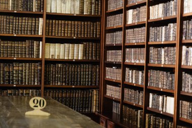 Eski bir ahşap kütüphanede, klasik atmosferi güçlendiren, sıcak ışıklandırmalı klasik deri kaplı kitaplar..