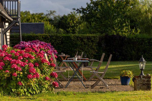 A patio with a table and chairs surrounded by pink flowers. Scene is peaceful and relaxing