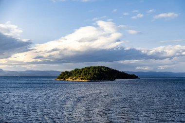 Dinamik bulutlarla dolu bir gökyüzünün altında, verimli ağaçlarla çevrili sakin bir ada..