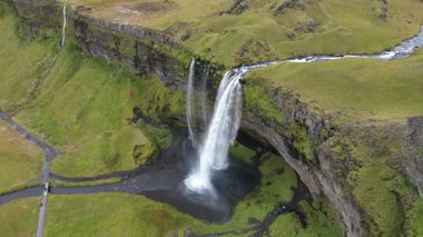 İzlanda insansız hava aracı görüntüsü. Seljalandsfoss şelalesi. Yukarıdan bir şelale görünüyor, arkasında yeşil çimenli bir tepe var..