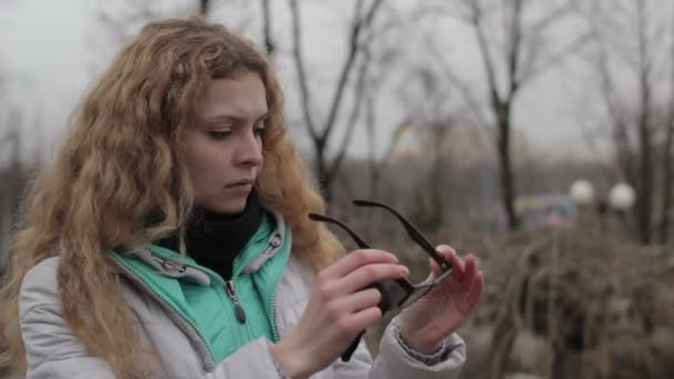 Chica limpieza gafas de lente en el parque en la ciudad — Vídeos de Stock