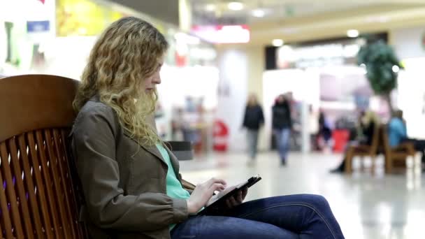 Νεαρή γυναίκα με δισκίο να καθίσει στον πάγκο στο εμπορικό κέντρο — Αρχείο Βίντεο