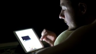 Geceleri yatakta tablet bilgisayar ile genç adam