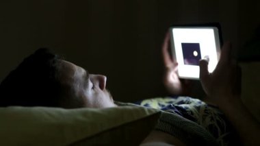 Geceleri yatakta tablet bilgisayar ile genç adam