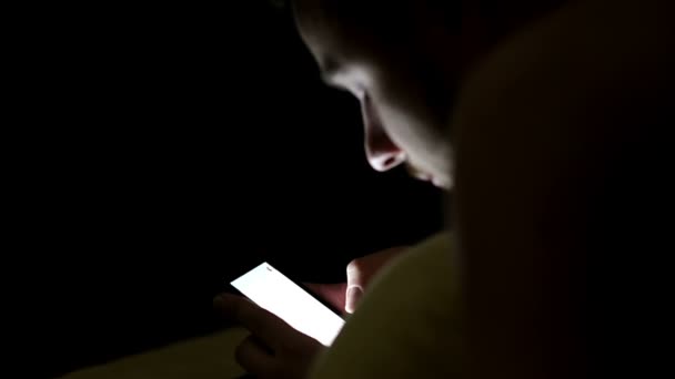 Jovem usando smartphone na cama sob cobertor à noite — Vídeo de Stock