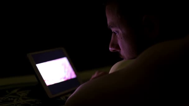 Młody człowiek z komputera typu tablet na łóżku w nocy — Wideo stockowe