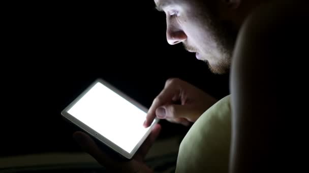 Hombre joven con tableta en la cama por la noche — Vídeos de Stock