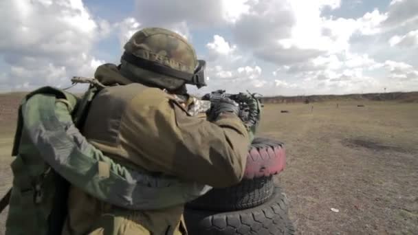 Um soldado com uma metralhadora num campo de tiro militar a disparar contra um alvo. . — Vídeo de Stock