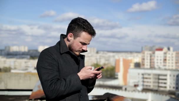 Homme utilisant le téléphone portable et l'écriture sms sur un toit de la maison — Video