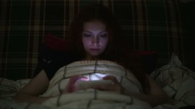 Geceleri evde yatakta yatarken smartphone kullanan genç kadın