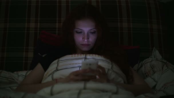 若い女性の夜、自宅のベッドに横になっているスマート フォンを使用して — ストック動画