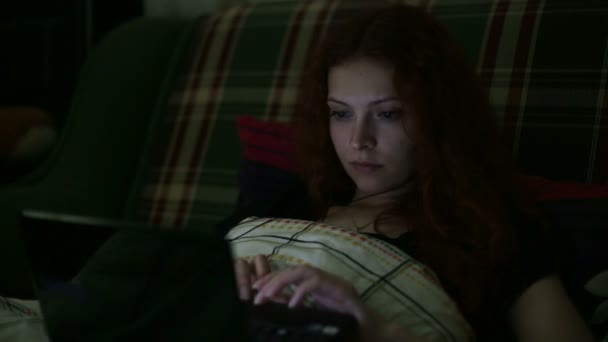 Молодая женщина с ноутбуком отвечает на звонки, лежащие на кровати дома ночью — стоковое видео
