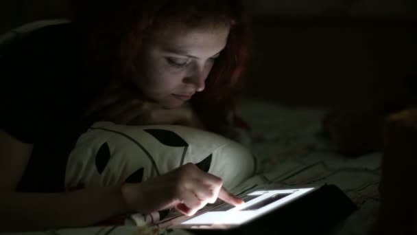 Молодая женщина с помощью планшета лежал на кровати дома ночью — стоковое видео