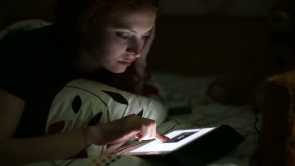 Jeune femme avec la tablette a reçu un message texte alors qu'elle était allongée sur un lit à la maison la nuit — Video