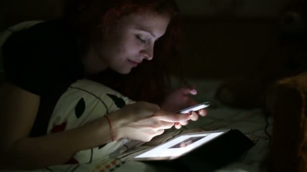 Mujer joven usando smartphone acostado en la cama en casa por la noche — Vídeos de Stock