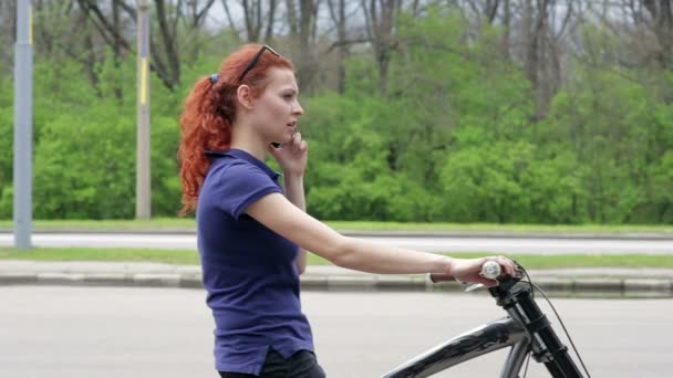 Молода жінка на велосипеді в парку розмовляє на мобільний телефон — стокове відео