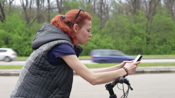 Girl sitting on the bike and texting on smartphone — Stock Video