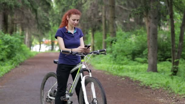 Девушка сидит на велосипеде и пишет смс на смартфоне — стоковое видео