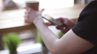 Genç kadın kapalı kentsel kafede oturan onun smartphone içme kahve ve kullanım
