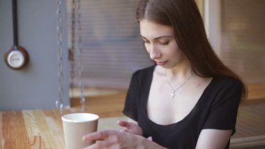 Genç kadın kapalı kentsel kafede oturan onun smartphone içme kahve ve kullanım