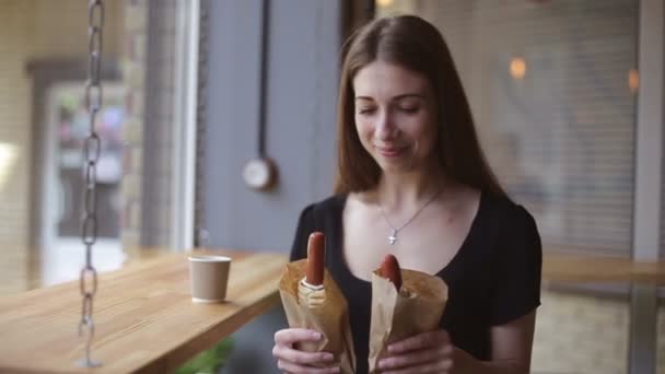 Hermosa chica comiendo un perrito caliente en un café . — Vídeos de Stock