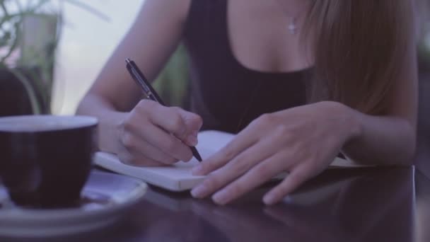 Красивая девушка сидит в уличном кафе и пишет заметки в блокноте — стоковое видео
