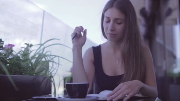 Linda chica sentada en la cafetería de la calle y escribiendo notas en el cuaderno — Vídeos de Stock