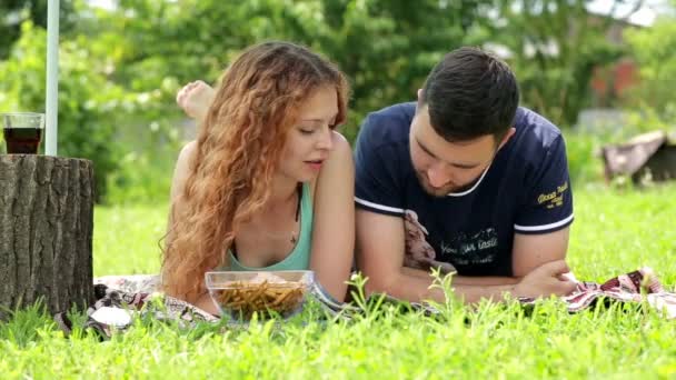 Un jeune couple lit le magazine et s'allonge sur l'herbe verte — Video