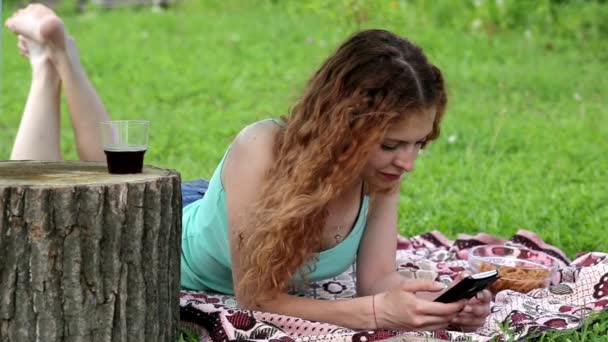 젊은 여성이 휴대 전화를 사용 하 고는 푸른 잔디에 누워 — 비디오