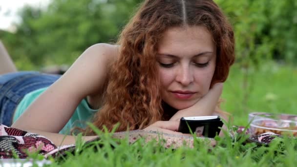 Mujer joven usando el teléfono móvil y acostado en la hierba verde — Vídeos de Stock