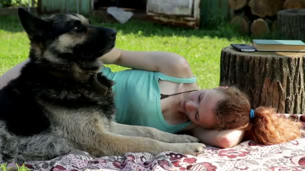 Een meisje ligt met een hond op het gras — Stockvideo