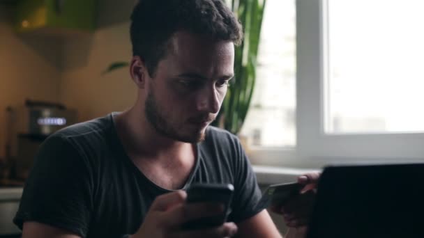 Mladý muž doma nákupy s kreditní kartou pomocí smartphone v kuchyni — Stock video