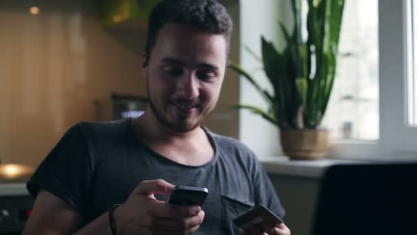 Joven en casa de compras con tarjeta de crédito usando teléfono inteligente en la cocina — Vídeos de Stock