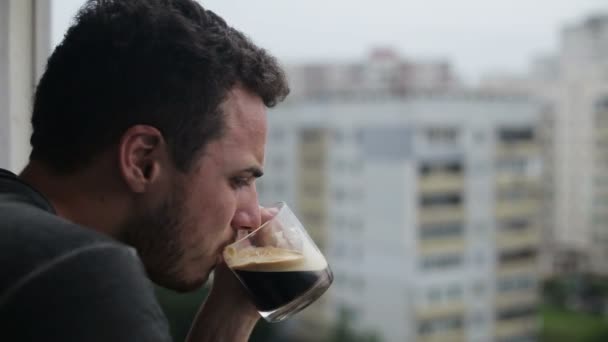 Jeune homme buvant du café et utilisant smartphone sur le balcon — Video