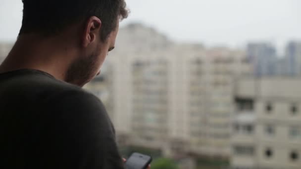 Jovem bebendo café e usando smartphone na varanda — Vídeo de Stock