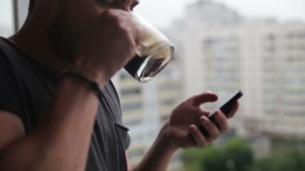 若い男がコーヒーを飲むとバルコニーでスマート フォンを使用して — ストック動画