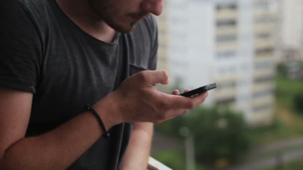 Young man drinking coffee and using smartphone on balcony — Stock Video