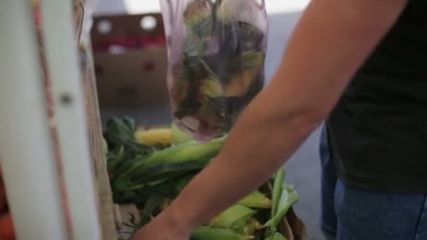 Человек покупает кукурузу на овощном рынке днем — стоковое видео