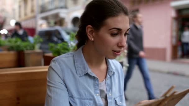 En leende kvinna på en restaurang med menyn i händer — Stockvideo