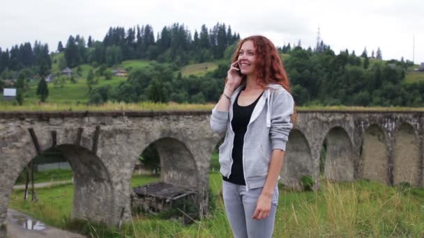 La chica habla por teléfono cerca del viejo viaducto en las montañas — Vídeos de Stock