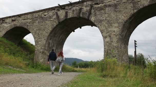 Happy couple walking along the road under the old viaduct — Stock Video