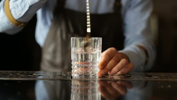 De barman draait het ijs in een glas met een lepel — Stockvideo