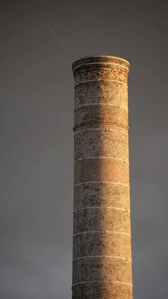 Endüstriyel baca, güzel gri gökyüzünün arka planında güneş ışınları duvarın tuğla dokusuna düşer. Simetri ve minimalizm, arkaplan ve doku